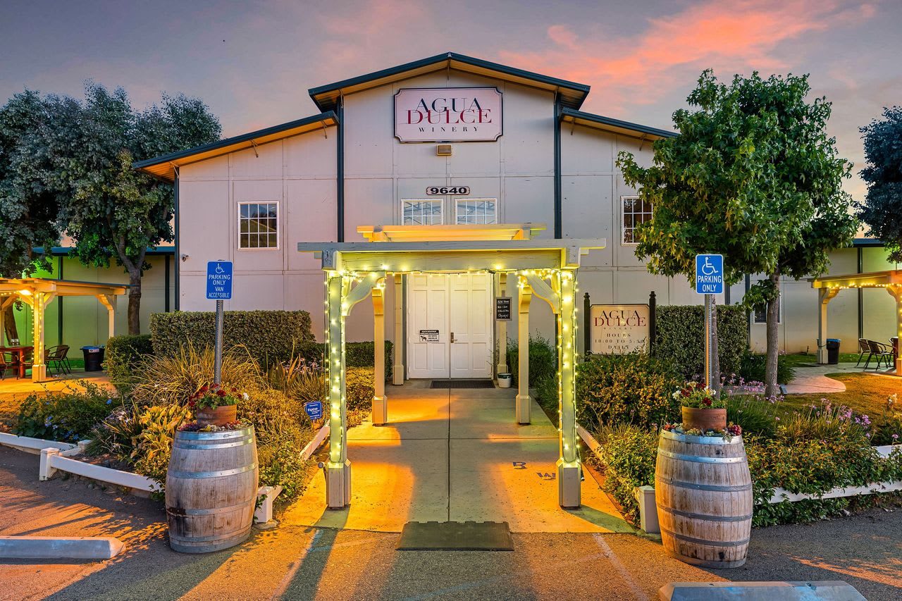 The tasting room building lit at night, with an arbor and wine barrels at the entrance
