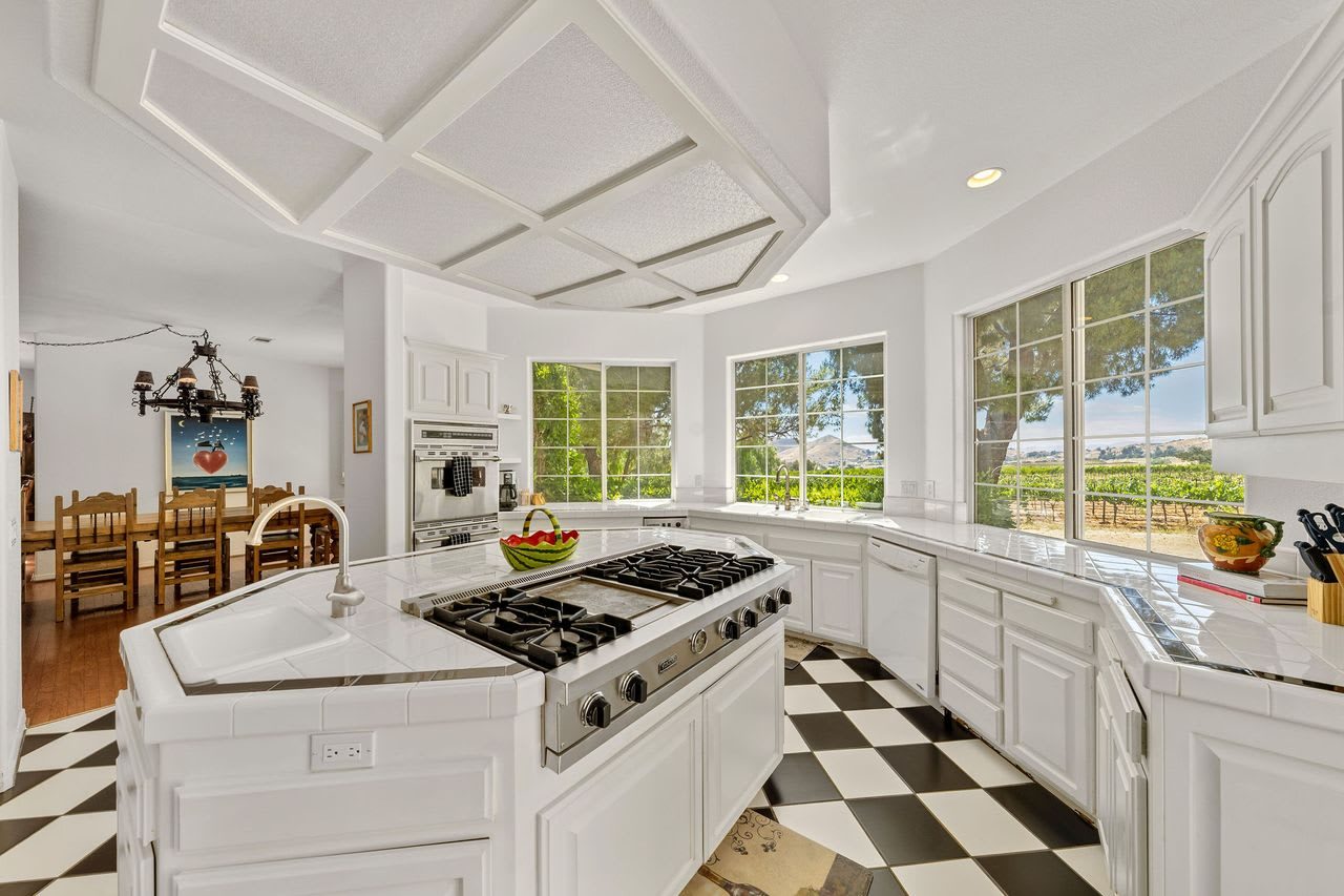 The kitchen, with white cabinetry, a range island and windows over the vineyard