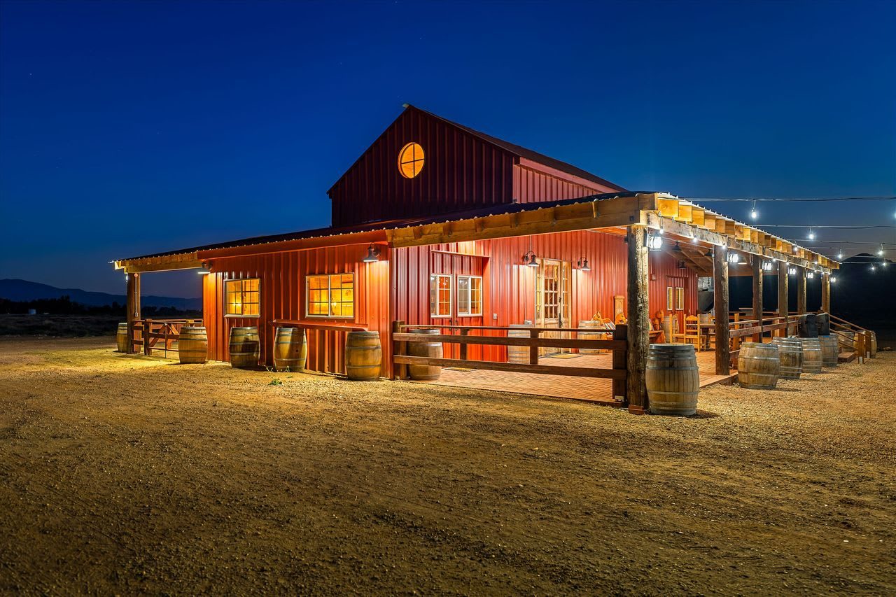The red events barn glowing at blue hour, strung with lights, wine barrels along the porch